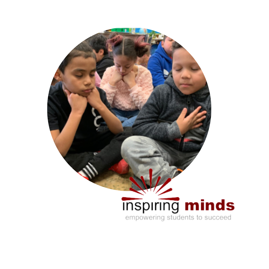 Children sitting on the ground smiling with the Inspiring Minds logo
