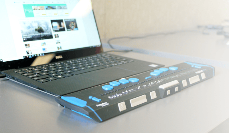 Background image of a computer with a braille keyboard connected.