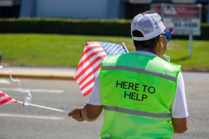 Volunteer helping to direct traffic with a green vest reading "Here to Help" on the back
