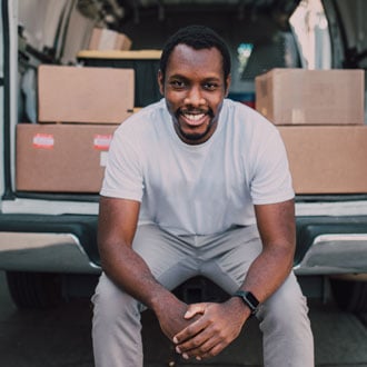 Volunteer sitting in the bed of a truck smiling with boxes of donated goods behind him