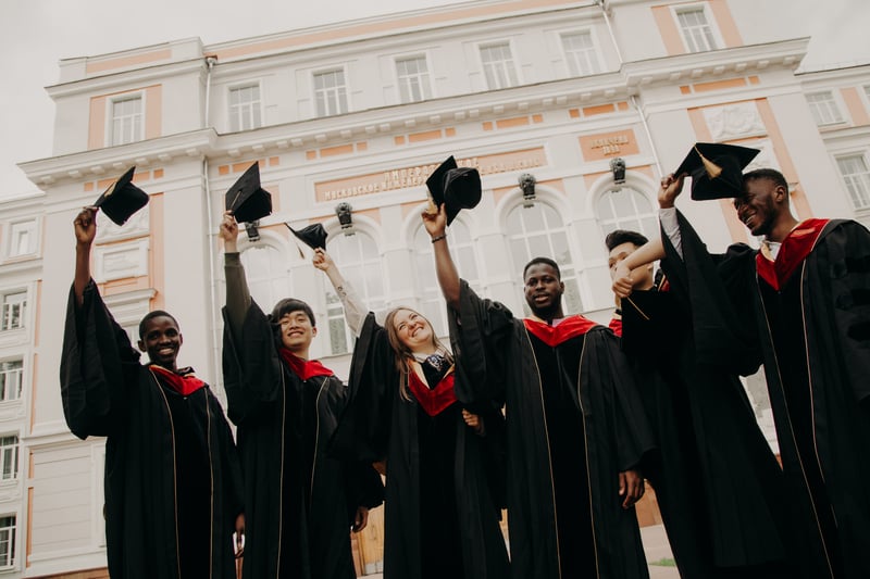 Six students who just graduated college smiling and holding their caps in the air