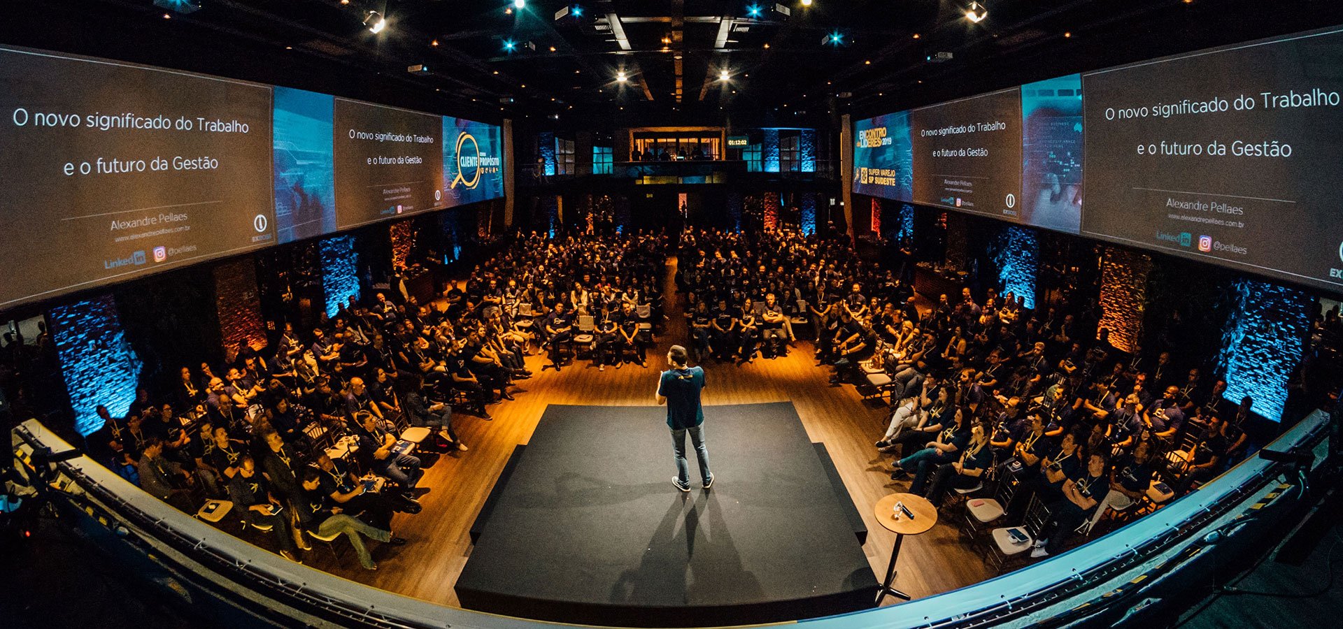 Crowd of people sitting in an auditorium watching a man presenting on a stage 