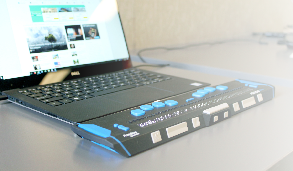 Background image of a computer with a braille keyboard connected.