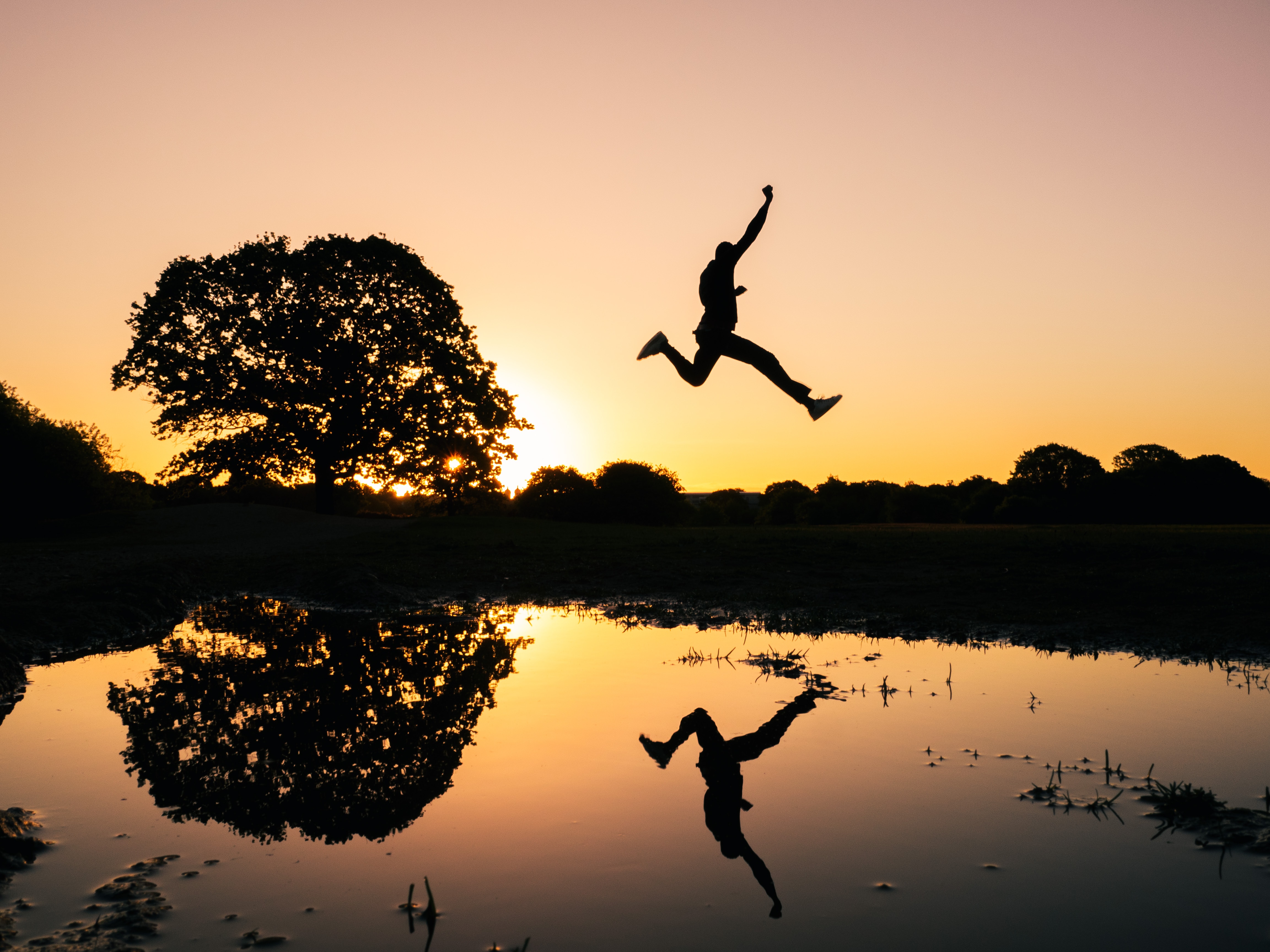 Volunteer leaping over a puddle with the sunset in the background